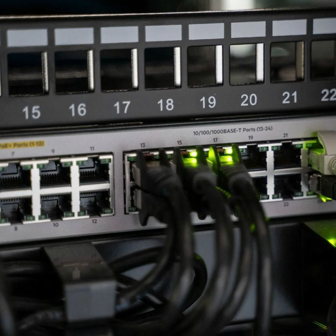 PoE Network Switches Close view of a PoE network switch with black Ethernet cables plugged into numbered ports below a patch panel